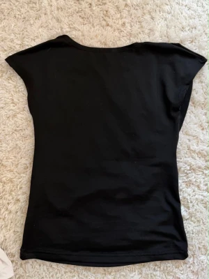Svart topp med öppen rygg - Snygg svart topp i stretchigt material med korta ärmar och en cool öppen ryggdetalj. Perfekt för dig som gillar en enkel men trendig look. Toppen har en figurnära passform och rund halsringning.