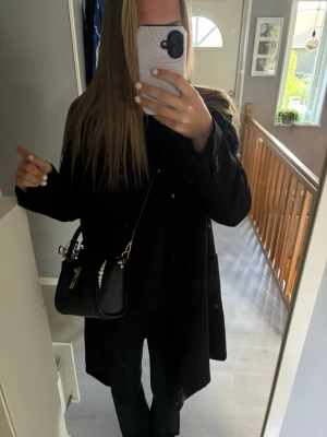 Kappa - Snygg svart kappa i rak modell med knäppning framtill och två fickor. Passar till allt. Stilsäker och enkel att matcha med olika outfits. Perfekt nu till hösten. Knappt använd 