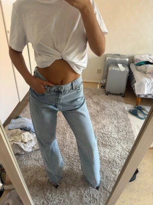Ljusblå raka jeans med hög midja - Säljer ett par ljusblå jeans med rak passform och hög midja. Jeansen har klassisk femficksdesign och är tillverkade i denim. Perfekta för en avslappnad och trendig look.