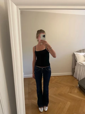 Mörkblå bootcut jeans med vita sömmar - Säljer ett par mörkblå bootcut jeans med tydliga vita kontrastsömmar och låg midja. Jeansen har klassiska fem fickor och en snygg passform som framhäver benen. Perfekta för dig som gillar en retroinspirerad look. Tror inte dom är använda en ända gång för passar inte resten av kläderna jag använder 