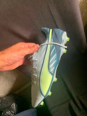Puma King fotbollsskor blå/neon - Snygga fotbollsskor från Puma King i ljusblått och neon-gult med vita detaljer. Skorna har snörning, låg profil och dobbar. De är 46 så passar bra för dig med stora fötter.
