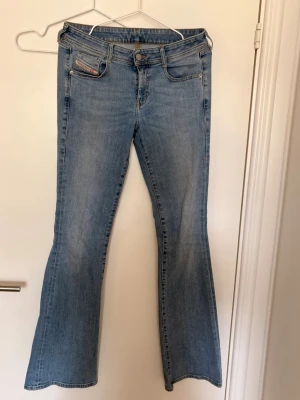 Ljusblå bootcut jeans - Säljer ett par ljusblå bootcut jeans med klassisk femficksmodell och utsvängda ben. Jeansen har normal midja och är tillverkade i mjukt denimtyg. Perfekta för dig som gillar retrovibbar och en avslappnad stil.