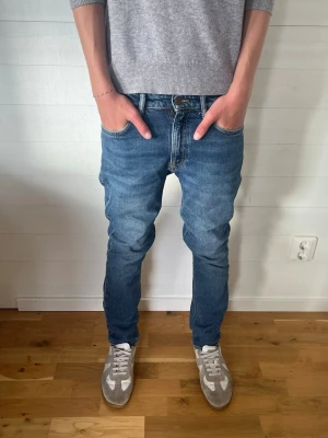 Blåa nudie jeans W25 L28 - Säljer ett par blå jeans i klassisk denim med snygga broderade detaljer på bakfickorna. Jeansen har normal midja, fyra fickor och stängs med knapp och dragkedja. Perfekta för en avslappnad och trendig look.🙌🙌