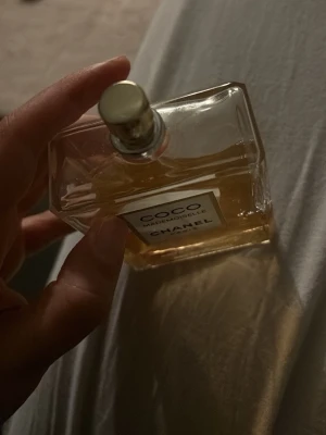 Coco Mademoiselle Eau de Parfum - Coco Mademoiselle Eau de Parfum från Chanel i en elegant, genomskinlig glasflaska med guldigt sprayhuvud. Doften är ikonisk och flaskan har en klassisk, stilren design med vit etikett och guldiga detaljer. Perfekt för dig som gillar lyxiga och tidlösa parfymer.