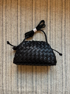 Svart flätad handväska med axelrem - Snygg svart handväska i flätad design med justerbar axelrem. Väskan har en mjuk, rundad form och stängs med dragsko i sidorna. Och passar perfekt för dig som gillar stilrena accessoarer.