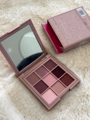 Matta ögonskuggspalett Huda Beauty - Säljer en matt ögonskuggspalett från Huda Beauty med nio nyanser i rosa, nude och bruna toner. Paletten har en fyrkantig form, spegel i locket och kommer i en stilren rosa plastförpackning. Perfekt för dig som gillar mjuka, matta färger till ögonen. Nypris 399kr! 🩷