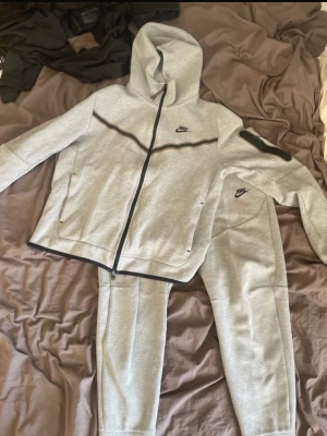 Grå mjukisbyxor från Nike - Säljer ett par grå mjukisbyxor från Nike med svart logga på vänster lår. Byxorna har dragsko i midjan, sidofickor och är tillverkade i mjukt sweatshirtmaterial. Perfekta för chill eller träning.