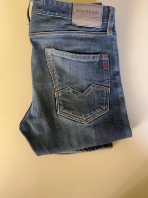 Blå Replay jeans slim - Snygga blå jeans från Replay med klassisk femficksdesign och raka ben. Jeansen har en diskret tvättad look, detaljerade sömmar på bakfickan och Replay-logga på både bakficka och framsida. Perfekta för en avslappnad och trendig stil.