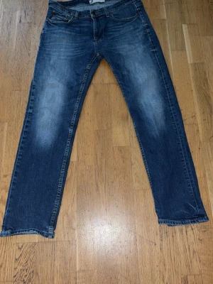 Blå raka jeans med slitningar - Snygga blå jeans med raka ben och diskreta slitningar på framsidan. Jeansen har klassisk femficksmodell och normal midja. Materialet är denim i bomull och färgen är mörkblå med ljusare partier för en trendig look.