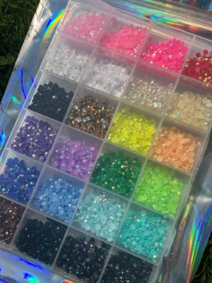 Bedezzel kit stor - Säljer ett kit med nageldekorationer i form av små runda stenar i olika färger som rosa, blå, grön, gul, svart och silver. Kommer i en praktisk ask med fack, samt verktyg och lim för enkel applicering. Perfekt för att skapa kreativa och färgglada nageldesigner.