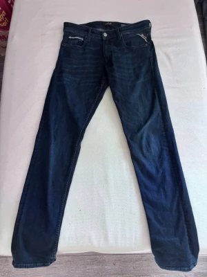 Replay jeans - Säljer ett par mörkblå jeans från Replay med raka ben och klassisk femficksmodell. Jeansen har snygga slitningar och kontrastsömmar samt en liten logga på fickan. Perfekta för en avslappnad och stilren look. Modellen grover. Storlek W29 : L 32