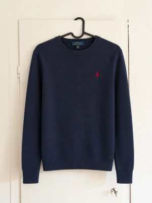 Stickad Ralph Lauren tröja - Säljer en stilren mörkblå stickad tröja från Polo Ralph Lauren med den ikoniska röda loggan på bröstet. En tidlös och lättmatchad tröja som passar perfekt året runt. ✔️ Klassisk modell ✔️ Broderad Polo-logga ✔️ Mjuk och bekväm passform ✔️ Passar både till vardag och finare tillfällen.               Bra skick men den är lite sliten och har en defekt!