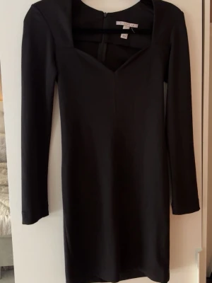 Svart långärmad klänning - En stilren svart klänning med lång ärm och v-ringad hals. Klänningen har en kroppsnära passform och är tillverkad i ett mjukt material som ger en elegant siluett. Perfekt för dig som gillar minimalistisk och klassisk stil.