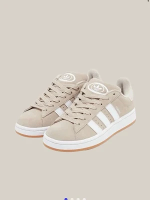 Beige Adidas sneakers med vita ränder - Snygga beige sneakers från Adidas med klassiska vita ränder på sidorna och vit sula med brun yttersula. Skorna har en låg profil, rund tå och är gjorda i mockaliknande material. Perfekta för en clean och stilren look. Dessa e använda fåtal gånger! 