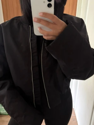 Svart oversized bomberjacka - Säljer en svart bomberjacka med oversized passform och lång ärm. Jackan har en klassisk rak form och dragkedja framtill. Perfekt för dig som gillar en enkel och stilren look.