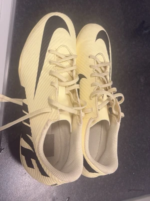 nike fotboll skor - Snygga gula Nike Mercurial fotbollsskor med svart swoosh och detaljer. Skorna har snörning och dobbar för bra grepp på planen. Tillverkade i syntetmaterial för lätt känsla och bra bollkontroll. Perfekta för dig som vill sticka ut på fotbollsplanen.