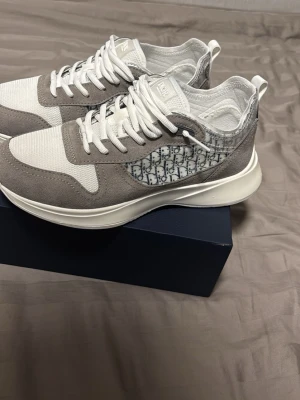 Gråvita sneakers med monogramdetaljer - Snygga sneakers i grått och vitt med mesh och mockadetaljer. Sidan har ett stilrent monogrammönster och skorna har vita snören samt en chunky vit sula. Perfekta för dig som gillar en clean och modern look.