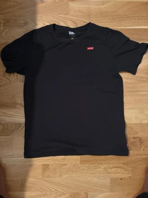 Levi’s Svart T-shirt – 16A / 176 cm - Säljer en svart Levi’s T-shirt i storlek 16A (176 cm). Tröjan är i fint skick och passar perfekt till vardags. Enkel att matcha med jeans eller shorts.  ✔️ Märke: Levi’s ✔️ Storlek: 16A / 176 cm ✔️ Färg: Svart ✔️ Bra skick ✔️ Skickas snabbt eller kan hämtas efter överenskommelse.  Hör gärna av dig om du vill ha fler bilder eller har frågor!