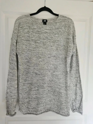 Ljusgrå melerad tröja från H&M - En stilren ljusgrå melerad tröja från H&M med rund halsringning och långa ärmar. Tröjan har en avslappnad passform och är tillverkad i ett mjukt, stickat material som passar perfekt till jeans eller kjol.