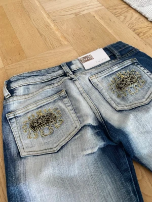 Vintage y2k crazy age bootcut jeans i storlek 36/26 - Säljer dessa blå lowwaist bootcut y2k jeans i märket crazy age med guldbrodyr på fickorna. Storleken är 36/26 och passar någon som är storlek S. Byxorna är lite slitna vid hälarna men annars är de i perfekt skick och jag säljer p.ga att de inte längre kommer till användning. 💗💗