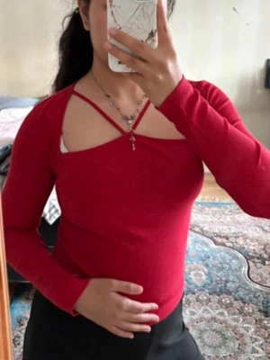 Röd långärmad topp med cut out - Trendig röd topp med långa ärmar och snygg cut out-detalj vid bröstet. Toppen har dekorativa band över axlarna som ger en unik look. Perfekt för dig som vill sticka ut lite extra.