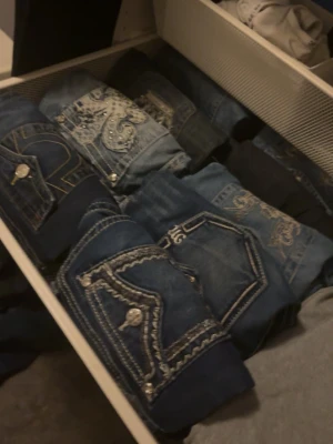 Blå jeans med broderade detaljer - SKRIV VID INTRESSE!!! Säljer flera par blå jeans med snygga broderade fickor och dekorativa sömmar. Flera olika tvättar och mönster, vissa med nitar och kontrastsömmar. Perfekta för dig som vill sticka ut med coola detaljer på jeansen.