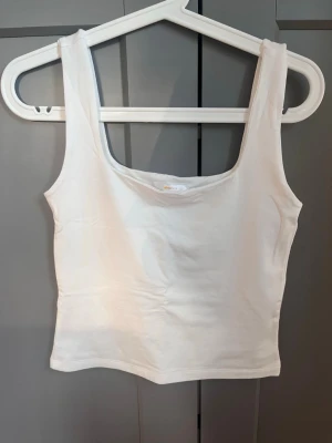 Vit linnetopp från Gina Tricot - Säljer en enkel och stilren vit linnetopp från Gina Tricot i storlek M. Toppen har breda axelband, rak passform och är tillverkad i mjuk bomullsmix. Perfekt att matcha med jeans eller kjol för en clean look. Använd endast en gång 