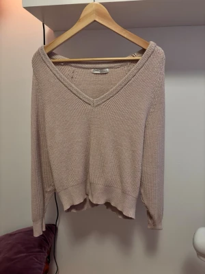 Beige stickad kofta Pull&Bear - Mysig beige stickad kofta från Pull&Bear med v-ringning och ribbade detaljer. Tröjan har avslappnad passform, långa ärmar och mjukt material som känns skönt mot huden. Perfekt för lager på lager och chill dagar.