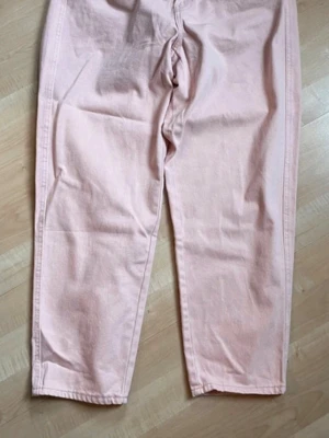Ljusa rosa Oanvända High Waist Twillbyxa - Säljer ett par ljusa rosa mom jeans med hög midja och avslappnad passform. Jeansen har ankellånga raka ben och resår i midjan för extra komfort. Perfekta för en trendig och avslappnad stil. Materialet är kraftigt bomullstyg.