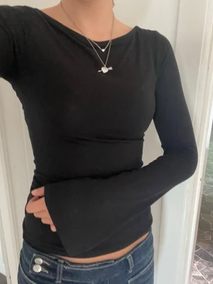 Svart långärmad tajt tröja med volang ärmar - Säljer en svart långärmad topp med tajt passform. Toppen har utsvängda ärmar och sitter tight över kroppen. Perfekt till jeans eller kjol för en stilren look.