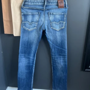 Blå Replay jeans slim fit - Snygga blå jeans från Replay i klassisk slim fit. Jeansen har coola detaljer på bakfickorna och slitningar framtill för en avslappnad look. De är tillverkade i mjukt denim och har normal midja. Perfekta för dig som gillar stilrena jeans med lite edge. Liten skada på sista bilden, märks knappt... Pris kan diskuteras.