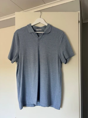 Ljusblå piké t-shirt med krage, Bläck - Säljer en stilren ljusblå piké t-shirt med klassisk krage och korta ärmar ifrån Bläck. Tröjan är gjord i mjukt bomullsmaterial och har en enkel, clean look utan mönster eller tryck. Perfekt för dig som gillar en avslappnad men ändå snygg stil.
