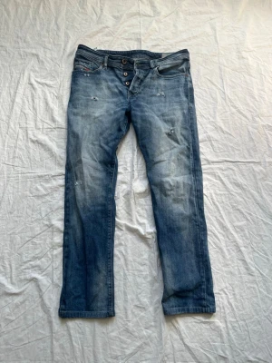 Blå slitna jeans med raka ben - Säljer ett par blå jeans med raka ben och slitna detaljer. Jeansen har knappgylf och klassiska fem fickor. Materialet är denim i bomull och de har en avslappnad passform som passar till det mesta.