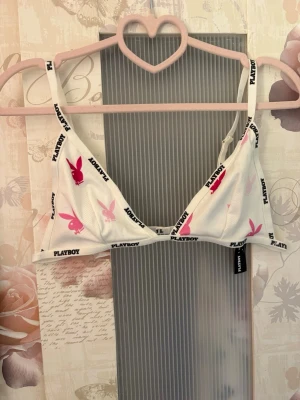 Vit Playboy x Missguided bralette - Vit bralette från Playboy x Missguided med svarta logotexter och rosa Playboy-kaniner i olika nyanser. Triangelformade kupor och justerbara axelband. Tillverkad i ribbad stretchig material för en bekväm passform.