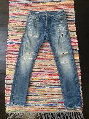 Blå Jack & Jones jeans - Säljer ett par blå jack & Jones  jeans med slitningar. Jeansen har en klassisk femficksmodell och raka ben. Materialet är denim i bomull och de har en cool, avslappnad look med tydliga slitdetaljer.