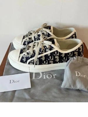 Dior Oblique sneakers i canvas - Snygga Dior Oblique sneakers i beige och marinblå canvas med klassiskt monogrammönster. Skorna har vita snören, gummisula och detaljer i vitt. Perfekta för dig som vill ha en lyxig och trendig look med streetwear-vibe.