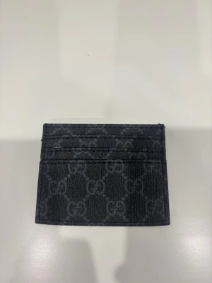 Svart kortfodral  - Snyggt svart kortfodral  med klassiskt GG-mönster i grått. Tillverkat i tåligt canvasmaterial och har flera fack för kort. Perfekt för dig som vill ha en stilren och lyxig accessoar i fickan.