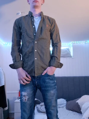 Grön skjorta från Ralph Lauren - Snygg grön skjorta från Ralph Lauren i slim fit-modell. Skjortan har klassisk krage, långa ärmar och knappar framtill. Tillverkad i bomull och har den ikoniska lilla loggan broderad på bröstet.