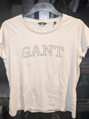 Vit kortärmad t-shirt från GANT - Säljer en vit t-shirt från GANT med klassisk rund hals och tryckt logga framtill. T-shirten är kortärmad och gjord i mjuk bomull, perfekt för en clean och enkel stil. Inga synliga fläckar eller defekter. Skapa en bundle för bättre pris