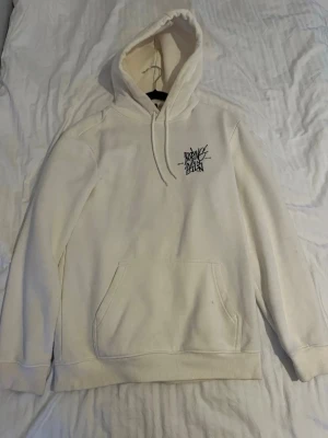 Vit hoodie från H&M med tryck - Säljer en vit hoodie från H&M i regular fit med svart grafiskt tryck på bröstet. Hoodien har huva med dragsko och en stor magficka framtill. Tillverkad i mjukt material, perfekt för en avslappnad stil.