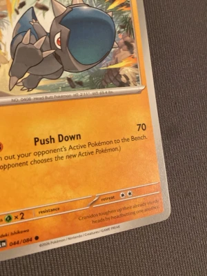 Pokémonkort Cranidos och Vullaby - Säljer två Pokémonkort: Cranidos med orange bakgrund och Vullaby med blå bakgrund. Cranidos har attacken Push Down och ett färgstarkt motiv med dinosaurietema. Vullaby har ett motiv av en fågelliknande Pokémon. Perfekt för samlare eller Pokémonfans!