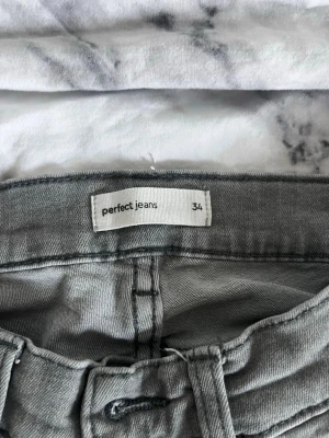 Grå bootcut jeans från Perfect Jeans - Snygga grå jeans från Perfect Jeans (gina tricot) i storlek 34. Modellen har bootcut-ben och klassisk femficksdesign. Jeansen har bälteshällor och stängs med knapp och dragkedja. Perfekta för dig som gillar en avslappnad men trendig look.
