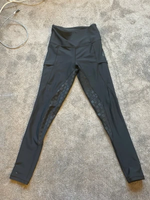 Svarta leggings från Maya Delorez - Snygga svarta ridleggings från Maya Delorez med hög midja och diskreta mönstrade detaljer längs benen. Tillverkade i ett stretchigt och bekvämt material som passar perfekt till träning eller chill. Fickor på sidorna för mobilen eller småsaker.