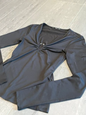 Svart långärmad topp med silverdetalj  - Snygg svart långärmad topp med v-ringning och en liten cut-out detalj framtill. Köpt här på Plick men passade tyvärr inte 