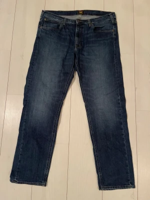Lee Jeans - Snygga mörkblå jeans från Lee med klassisk rak passform. Jeansen har fem fickor, guldfärgade sömmar och bälteshällor. Tillverkade i slitstark denim som passar perfekt till en avslappnad stil. Storlek W36 L32