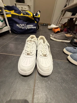 Vita Nike airforce - Säljer ett par klassiska vita sneakers i lågt modell med perforerad tå och vita skosnören. Skorna har en enkel och stilren design med diskreta sömmar och är tillverkade i skinn. Perfekta för dig som gillar en clean och tidlös look.
