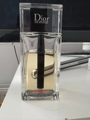 Dior Homme Sport parfym - Dior Homme Sport parfym i en stilren, rektangulär glasflaska med svart och silverfärgad detalj. Flaskan har tydlig Dior-logga och rymmer 125 ml. Doften är maskulin och modern, perfekt för dig som gillar exklusiva parfymer.