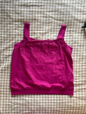 Rosa linne med broderi och breda band - Snyggt rosa linne med breda axelband och broderade detaljer upptill. Linnet har små prickar i samma färg över hela framsidan och en söt spetskant vid halsen. Perfekt för en trendig och avslappnad look. Materialet är mjukt och bekvämt  bomull.