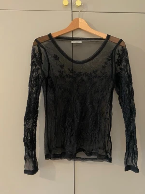 Svart meshblus från Hunkydory - Säljer en svart meshblus från Hunkydory med lång ärm. Den är transparent och har broderade blommönster över hela plagget. Storlek S/M