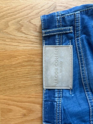 Jacob Cohën Nick Stl 33 - Blå jeans från Jacob Cohën med beige patch logga. strl 33. Har använts normalt mycket för att ha haft dom i några månader, men dom har varit lite för små (varför jag säljer dem) så fick laga grenen en gång som syns på insidan men utsidan är som mycket bra skick. Överlag är dom i mycket bra skick och parfymeringen sitter fortfarande i, känslan av jeansen är relativt nya. Tveka inte på att skriva om du undrar något om jeansen.